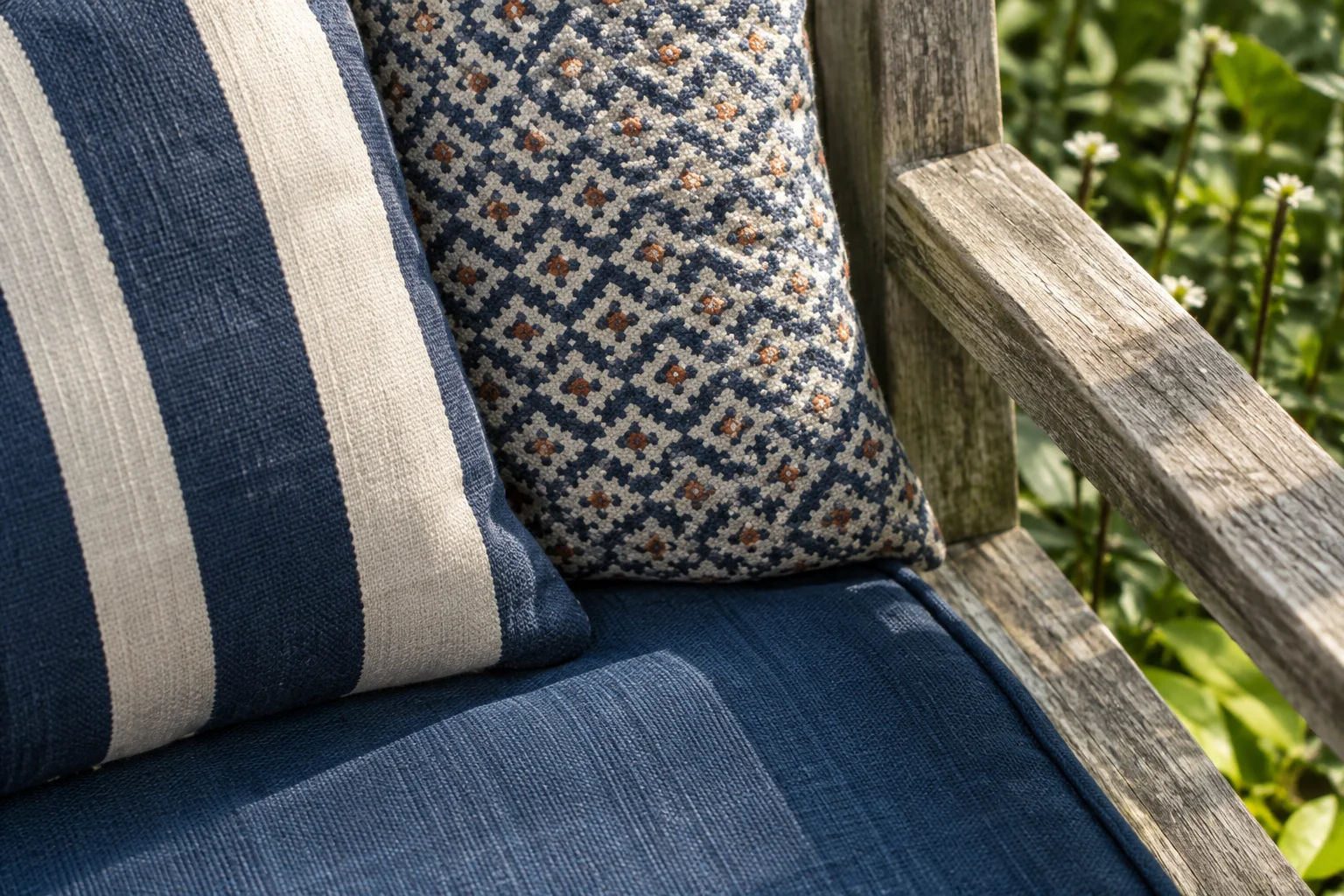 Brede blauwe strepen, een fijne geometrische print en een effen blauw kussen delen een kleur op een verweerde houten zitplek.