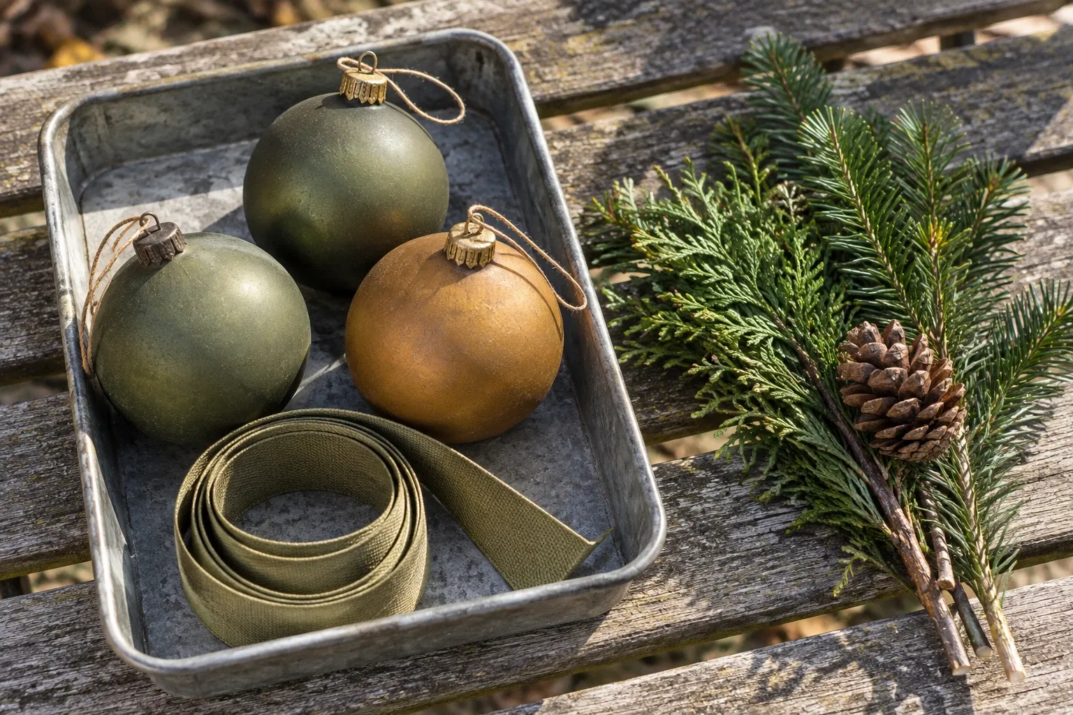 Matte outdoor ornaments lie separately from cut evergreen foliage on a worn wooden bench, ready to be sorted after the display is dismantled.