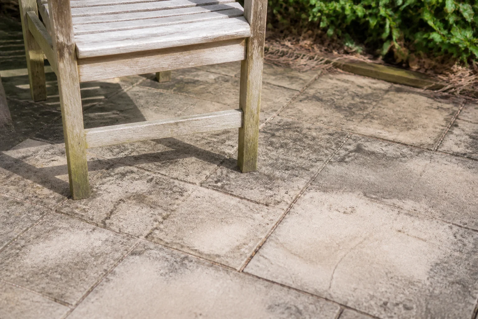 The front edge and feet of a garden chair rest on worn paving with clear ground in front.
