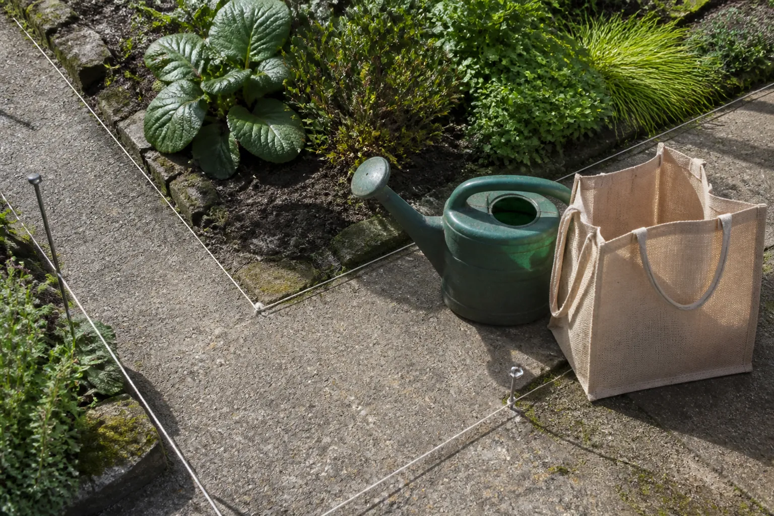 A watering can and shopping bag sit beside a path corner marked with string, showing the clear carrying width.