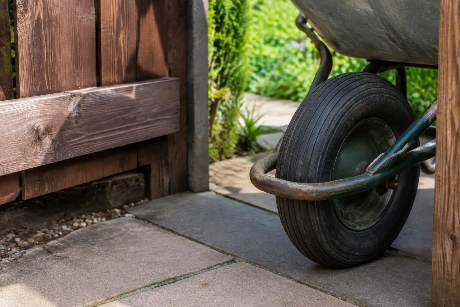 A worn wheelbarrow tire sits at a timber garden-gate threshold, showing the access that renovation work must use.