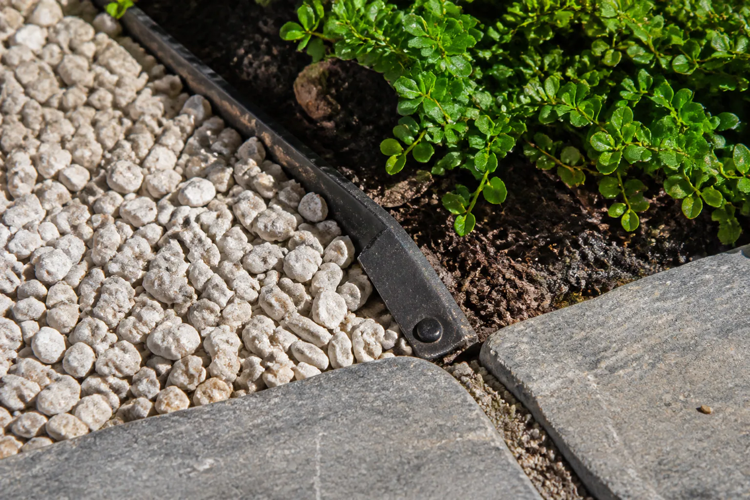 Pale gravel, a weathered paver and low planting meet at a simple fastened metal edge.