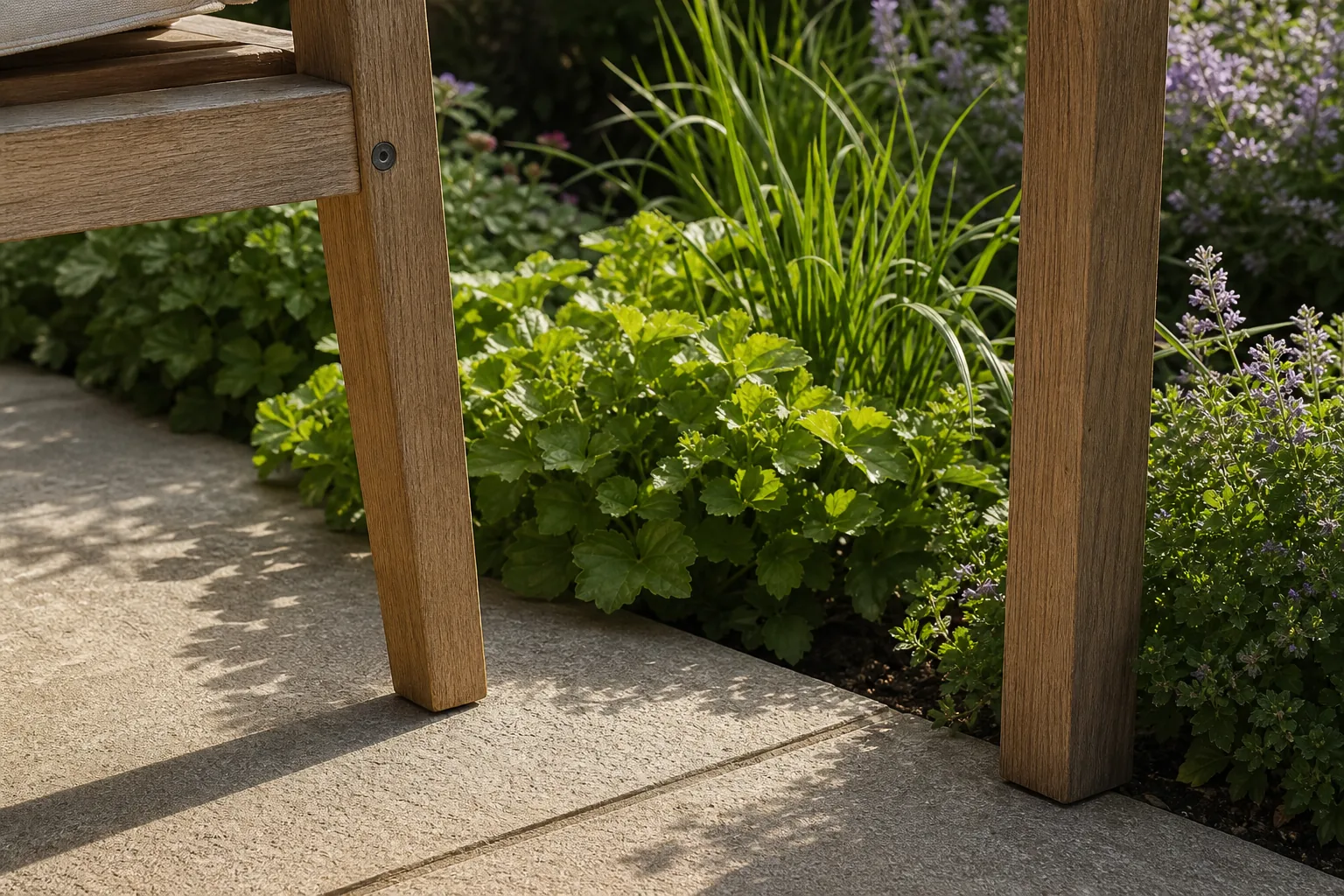 The feet of simple wooden outdoor furniture sit on stable paving immediately beside a lush planted edge.