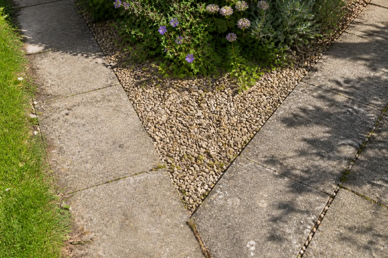 Two worn paved routes meet beside gravel and a planted edge in an ordinary garden.